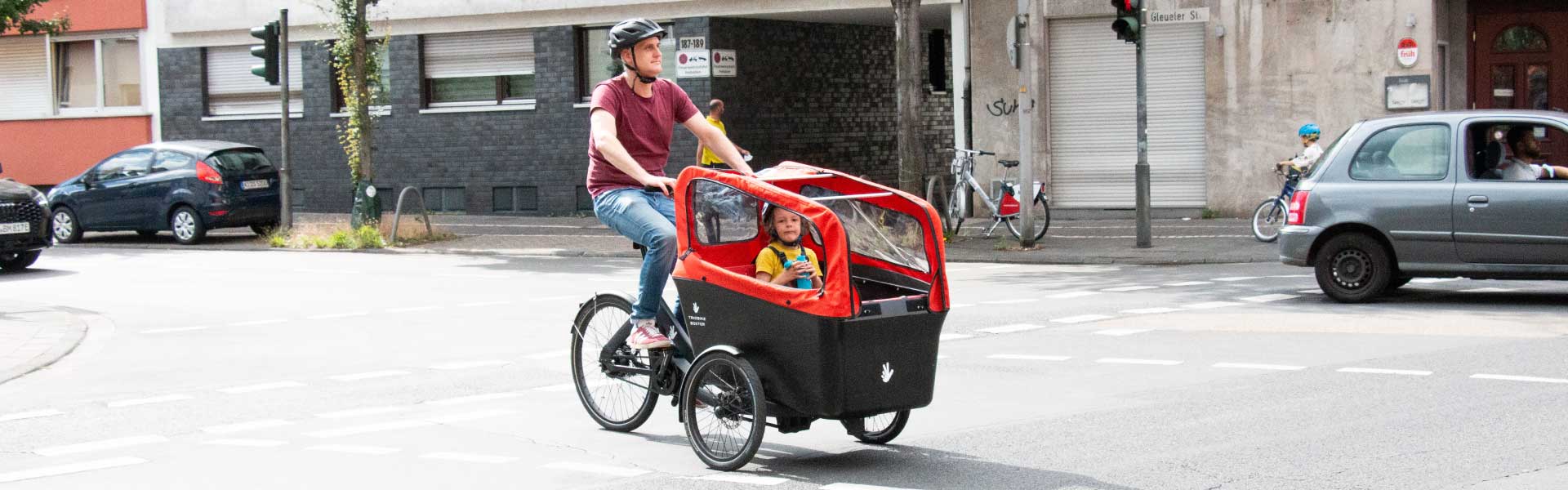 Mann fährt mit Sohn und dem Triobike Boxter-e über die Straße