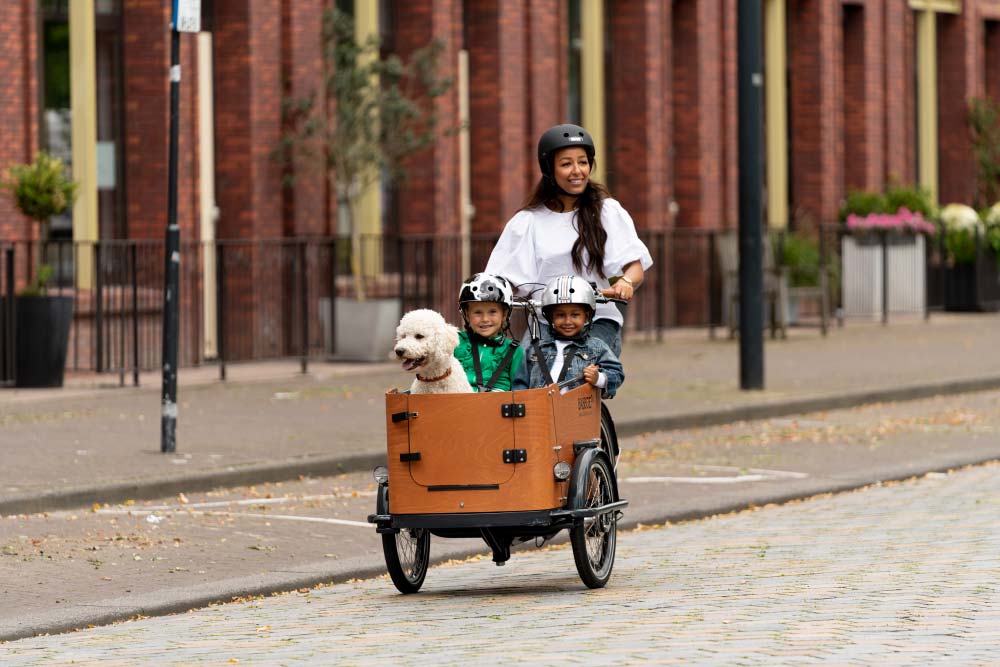 Frau fährt mit dem Lastenrad von Babboe und 2 Kindern sowie einem Hund durch die Stadt