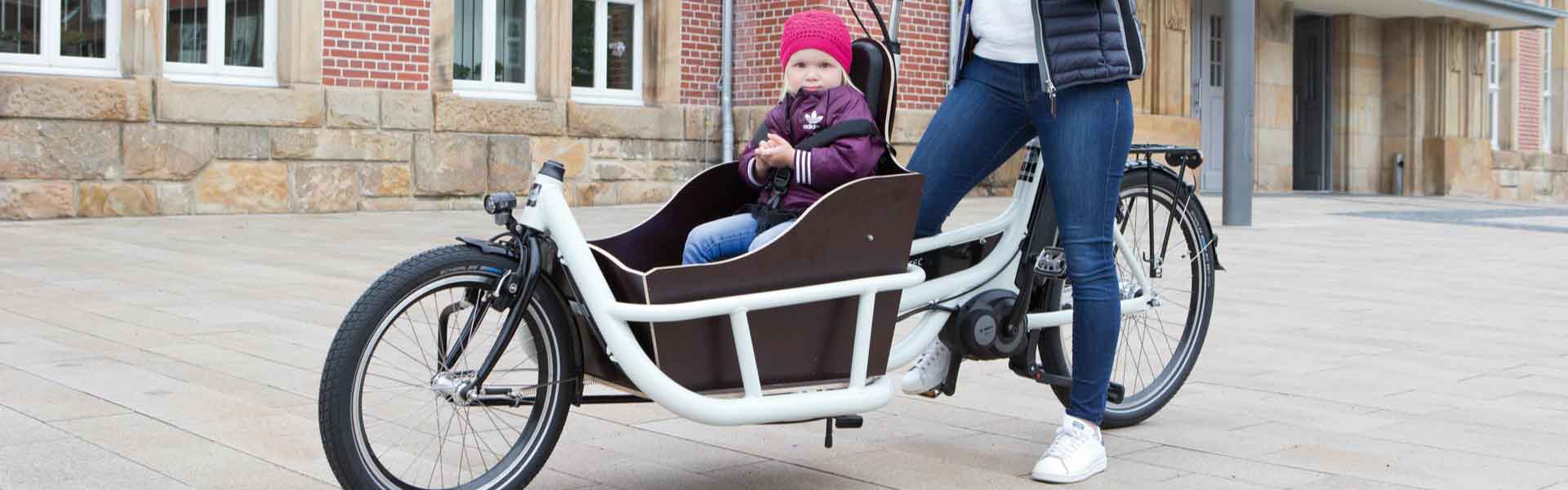 Frau steht mit dem pfautec Carrier und ihrem Kind vor einem Gebäude