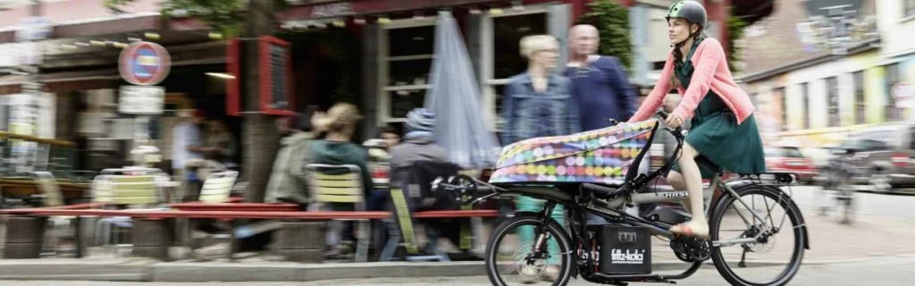 Frau fährt mit dem HASE BIKES Lastenrad PINO Steps durch die Stadt