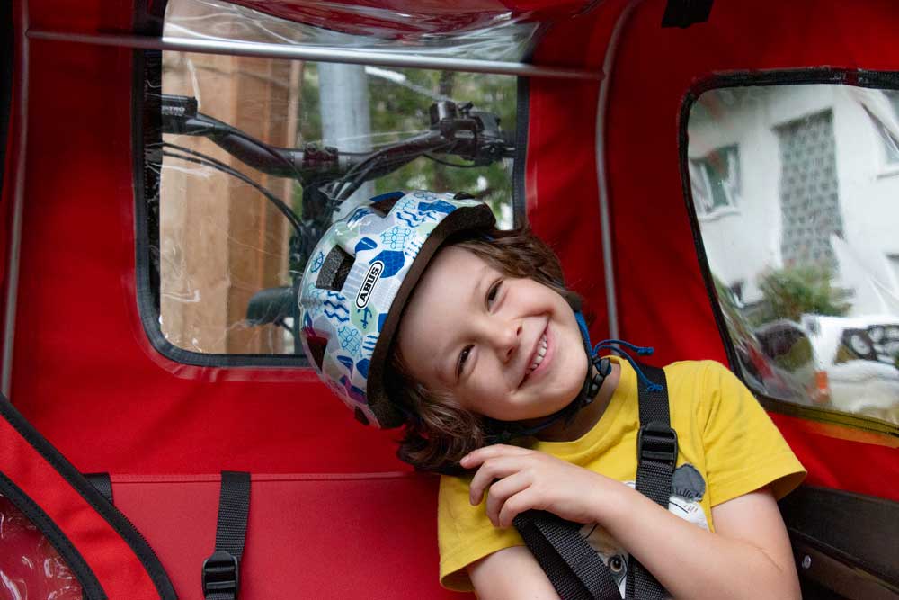 Junge sitzt mit Helm im Lastenfahrrad von Triobike