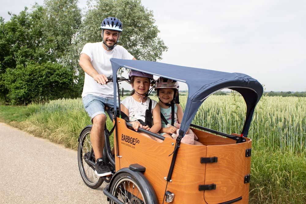 Ein Mann fährt das Babboe Go Mountain, in der Box sitzen seine zwei Töchter