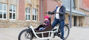 Eine Frau steht vor dem Lastenrad von pfautec und in Kind sitzt vorne in der Transportbox