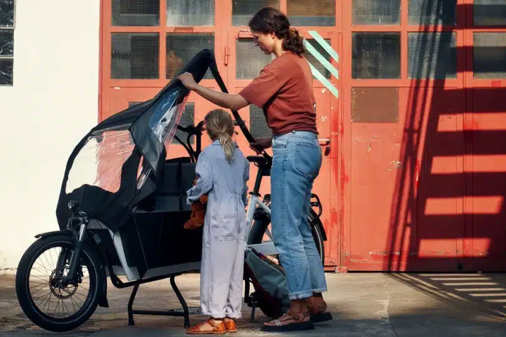 Eine Frau räumt  mit ihrem Kind das Transporter Cargobike ein